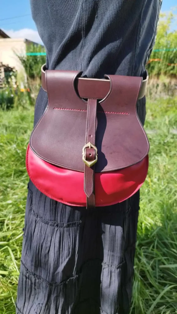 Escarcelle d'inspiration médiévale, en cuir, couleur chocolat et rouge. Fermeture par boucle en laiton. S'attache à la ceinture grâce à des passants.